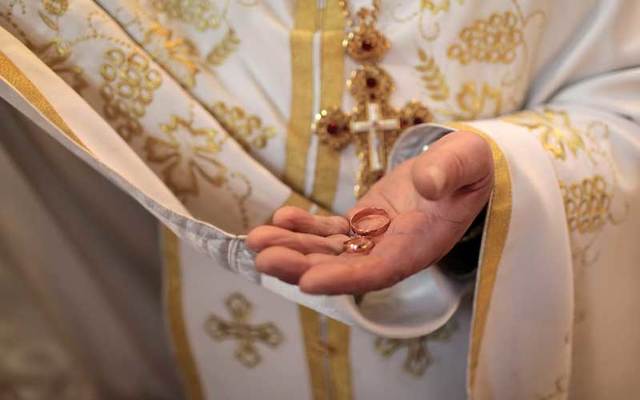 A priest holds wedding rings in his hand.